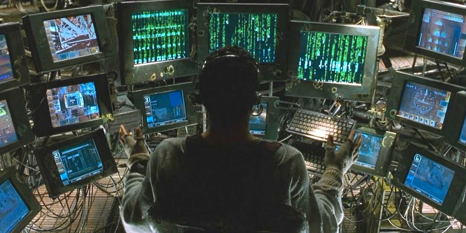 an image from the movie THE MATRIX, where we see a man sitting at a variety of computer terminals with many wires.